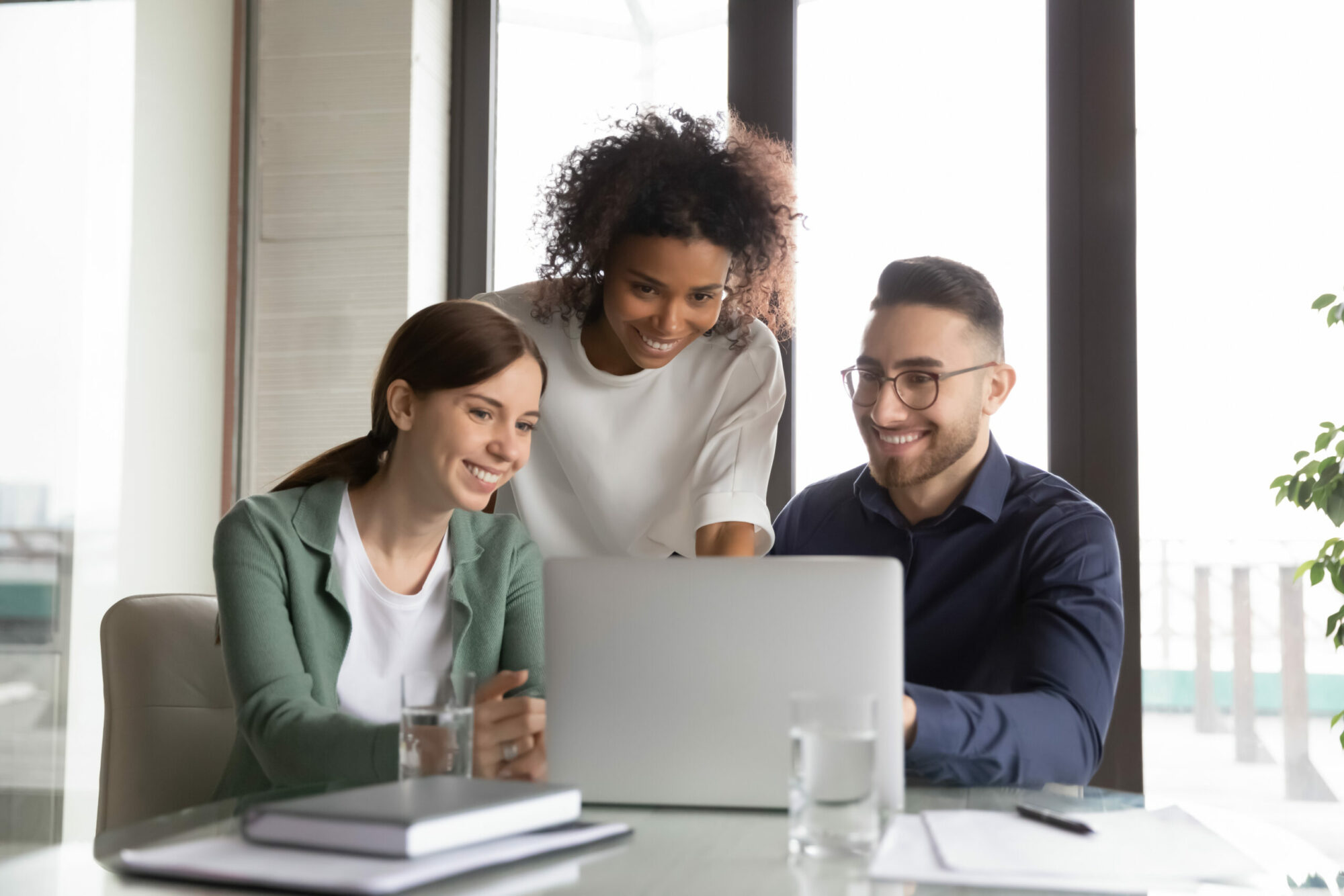 Three happy diverse colleagues working on project together, using laptop